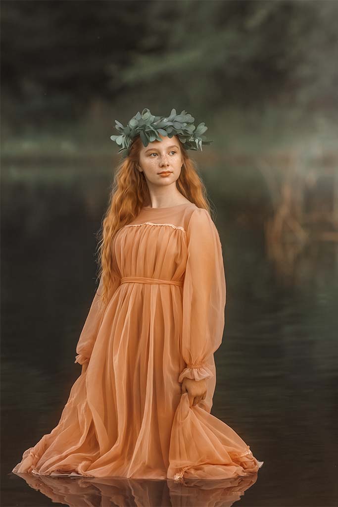 dziewczynka w pomarańczowej tiulowej sukience z zielonym wiankiem na głowie stojąca w wodzie