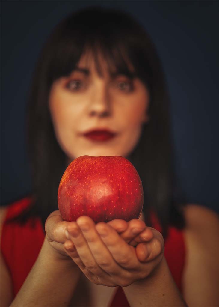 portret twarzy kobiety z wyciągniętymi rękami w których trzyma jabłko