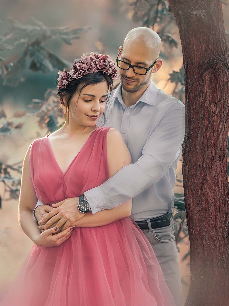 kobieta w różowej sukni stojąca pod drzewem oparta o mężczyznę
