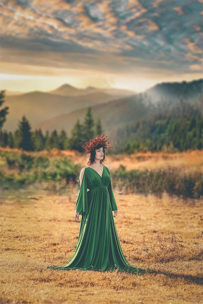 kobiet stojąca na łące w zielonej sukience i czerwonym wianku na głowie w tle góry
