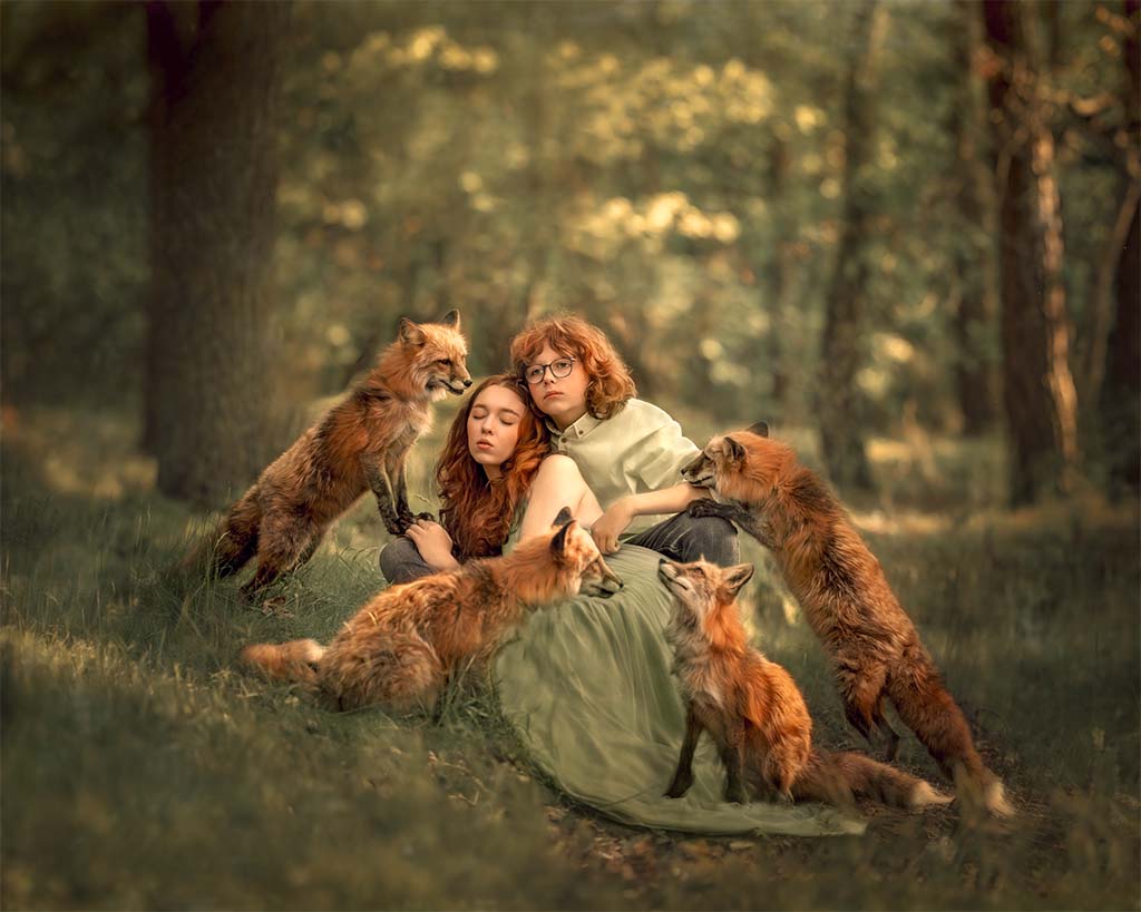 dziewczynka z chłopcem siedząca na leśnej drodze, obok nich 4 lisy