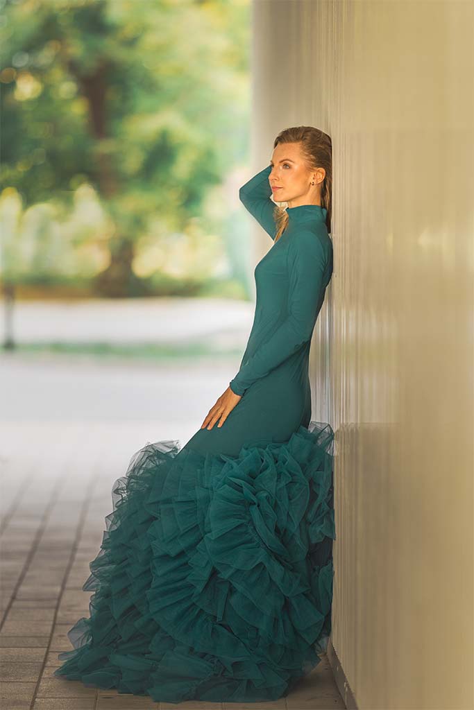 kobieta w zielonej sukni pozuje oparta o ścianę