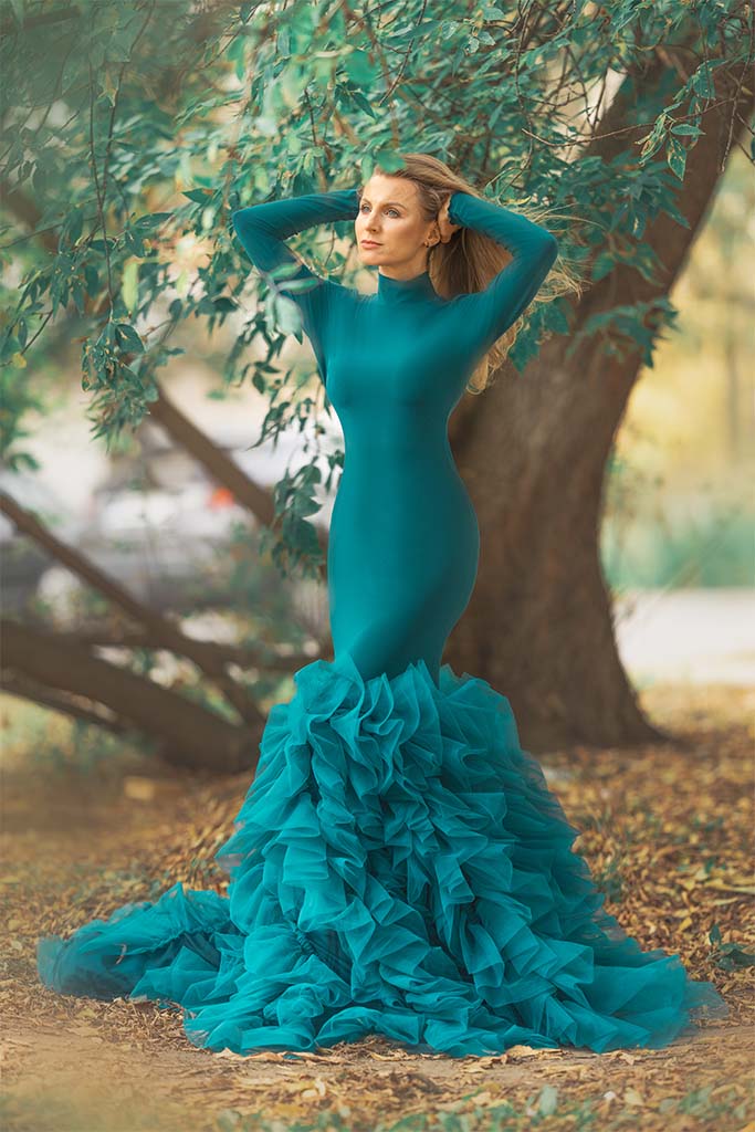 kobieta w zielonej sukni pozuje pomiędzy drzewami