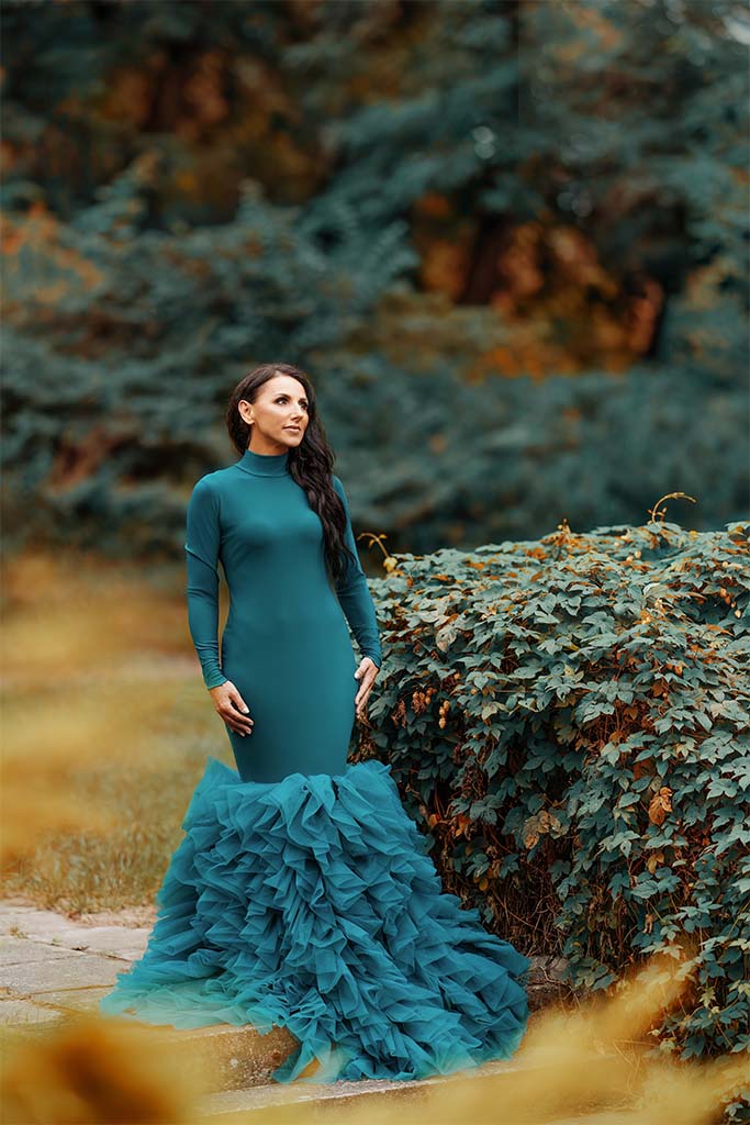 kobieta w zielonej sukni pozuje pomiędzy drzewami