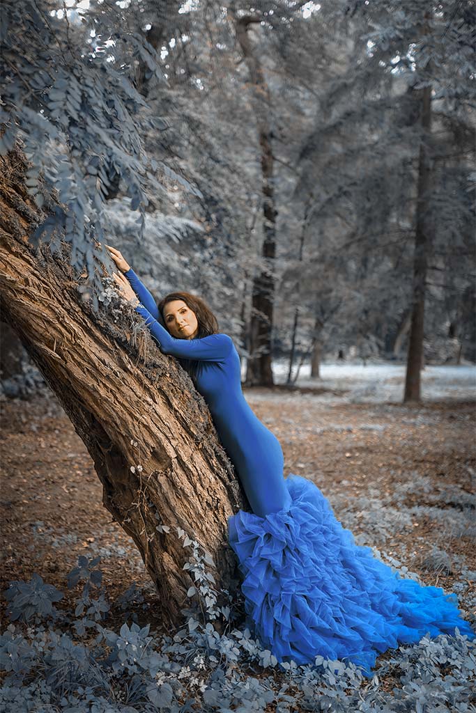 kobieta w granatowej sukni pozuje pomiędzy drzewami