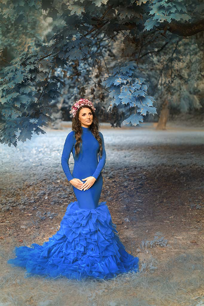 kobieta w granatowej sukni pozuje pomiędzy drzewami