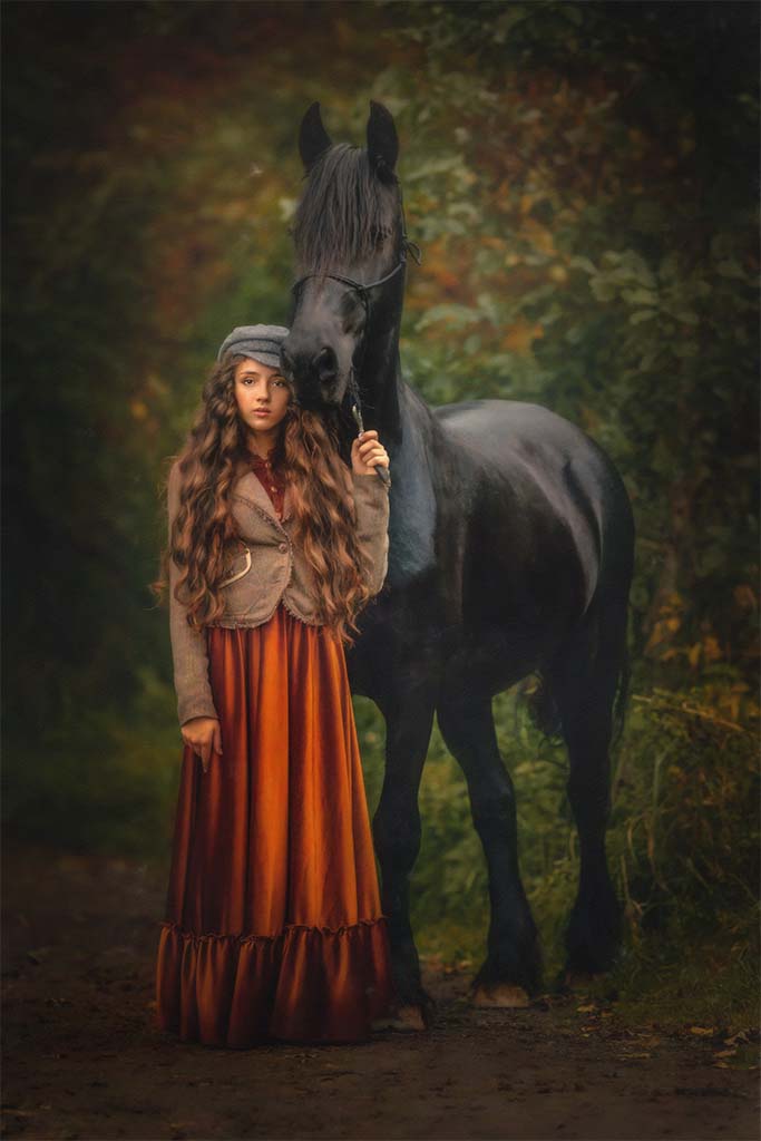 Młoda dziewczynka stojąca na drodze leśnej z czarnym koniem rasy fryzyjskiej